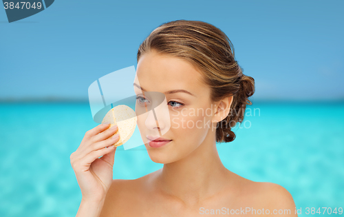 Image of young woman cleaning face with exfoliating sponge