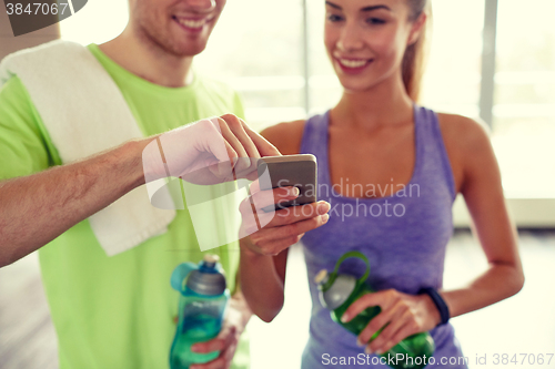 Image of happy woman and trainer showing smartphone in gym