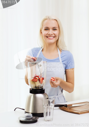 Image of smiling woman with blender preparing shake at home