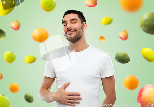 Image of happy full man touching tummy over falling fruits