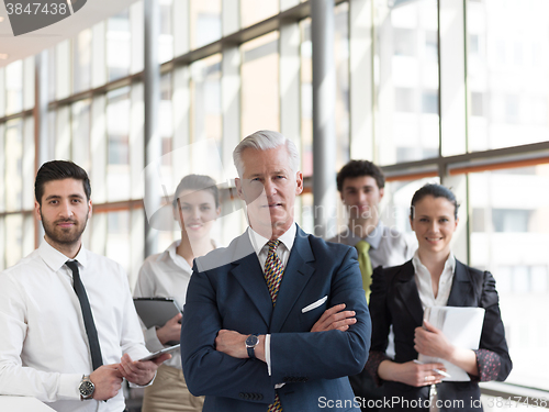 Image of portrait of senior businessman as leader  with staff in backgrou