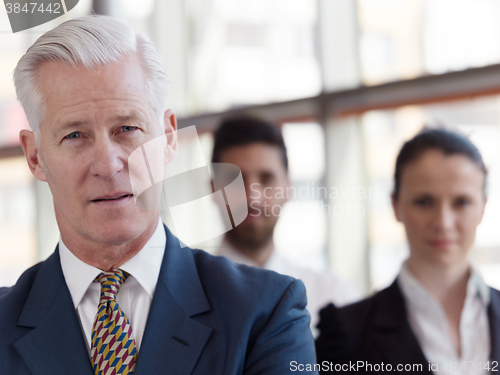 Image of portrait of senior businessman as leader  with staff in backgrou