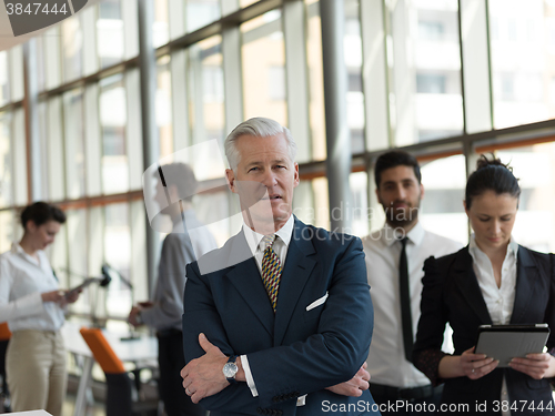 Image of portrait of senior businessman as leader  with staff in backgrou