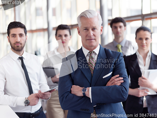 Image of portrait of senior businessman as leader  with staff in backgrou