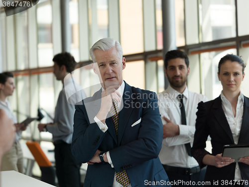 Image of portrait of senior businessman as leader  with staff in backgrou