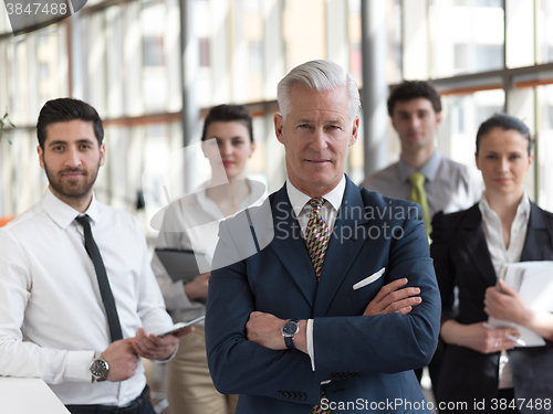 Image of portrait of senior businessman as leader  with staff in backgrou