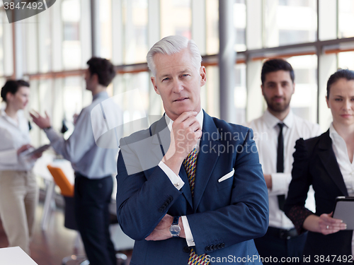Image of portrait of senior businessman as leader  with staff in backgrou