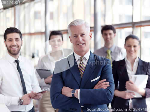 Image of portrait of senior businessman as leader  with staff in backgrou