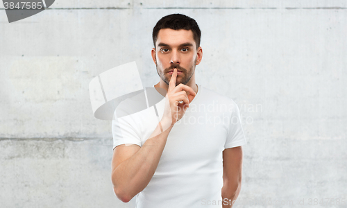 Image of young man making hush sign over gray wall