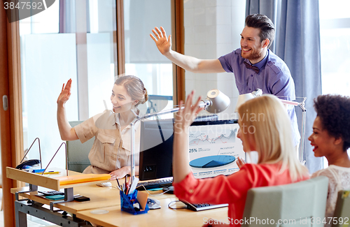 Image of happy creative team waving hands in office