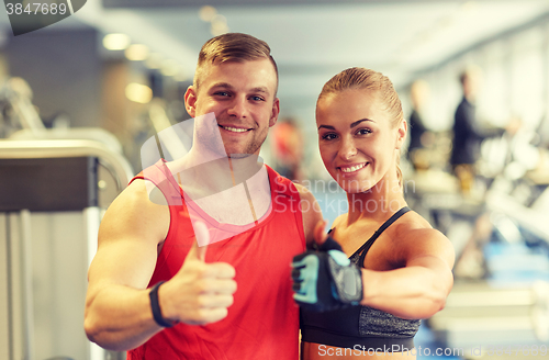 Image of smiling man and woman showing thumbs up in gym