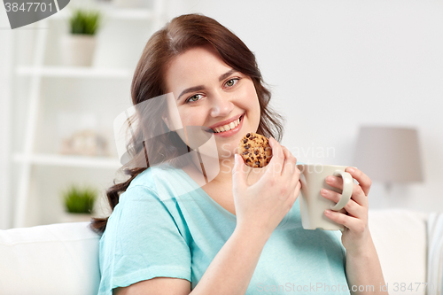 Image of happy plus size woman with cup and cookie at home