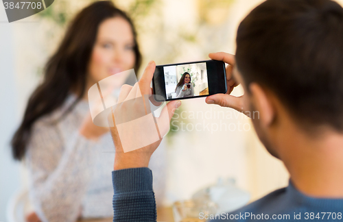 Image of man taking picture of woman by smartphone at cafe