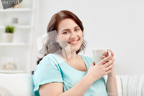 Image of happy plus size woman with cup of tea at home