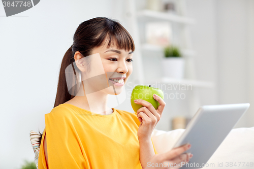 Image of happy asian woman with tablet pc and apple at home