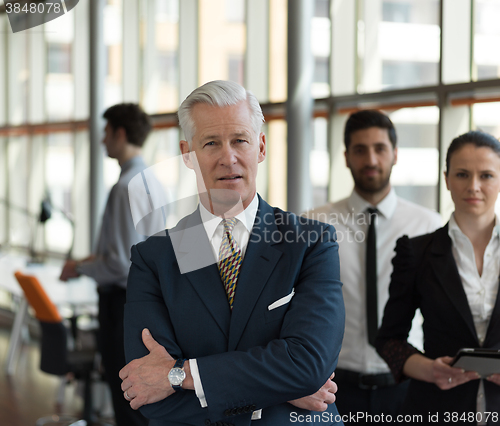 Image of portrait of senior businessman as leader  with staff in backgrou