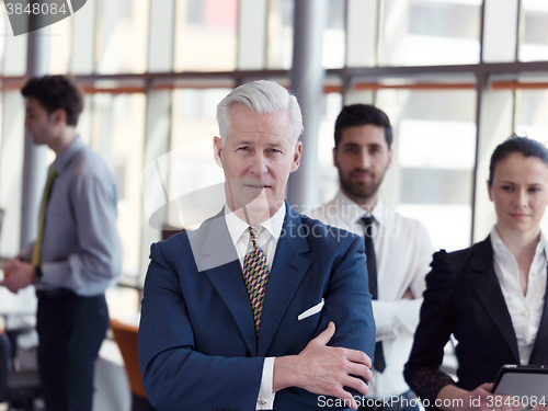 Image of portrait of senior businessman as leader  with staff in backgrou