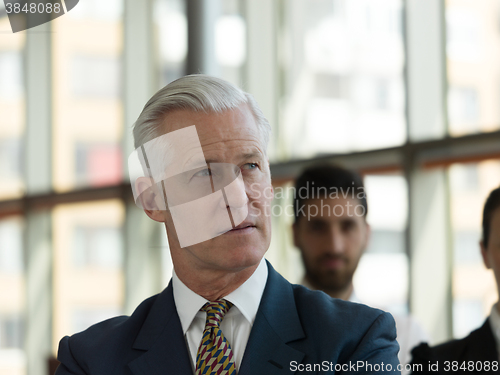 Image of portrait of senior businessman as leader  with staff in backgrou
