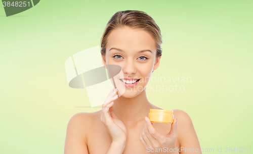 Image of happy young woman applying cream to her face
