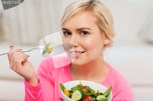 Image of smiling young woman eating salad at home