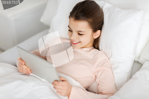 Image of happy girl lying in bed with tablet pc at home