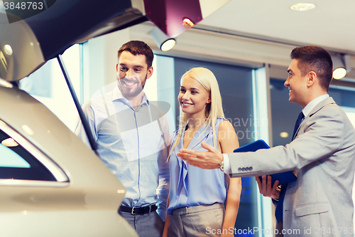 Image of happy couple with car dealer in auto show or salon