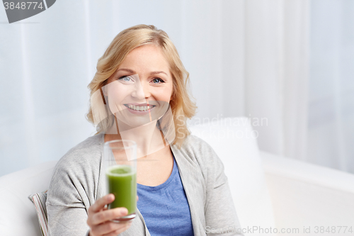 Image of happy woman drinking green juice or shake at home