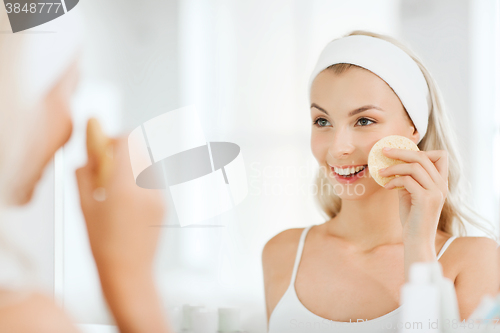 Image of young woman washing face with sponge at bathroom