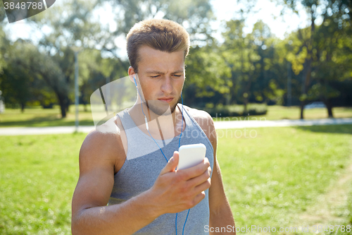 Image of young man with earphones and smartphone at park