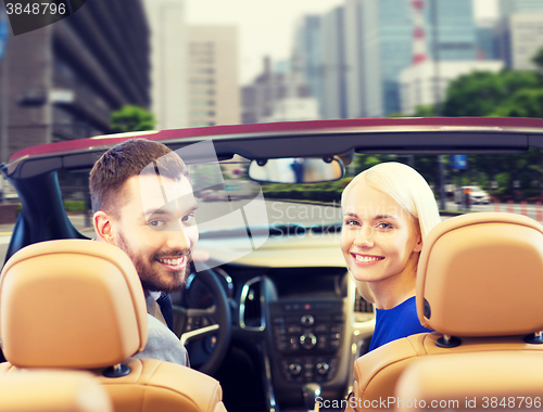 Image of happy couple driving in cabriolet car over city