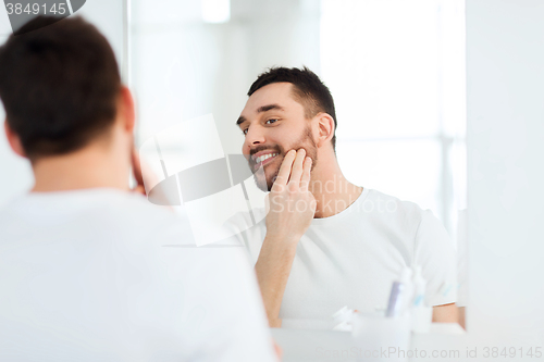 Image of happy young man applying cream to face at bathroom