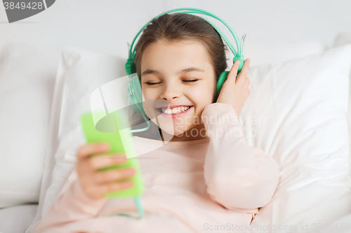 Image of happy girl lying in bed with smartphone at home