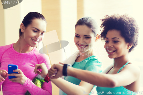 Image of happy women showing time on wrist watch in gym