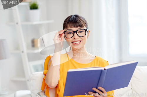 Image of smiling young asian woman reading book at home