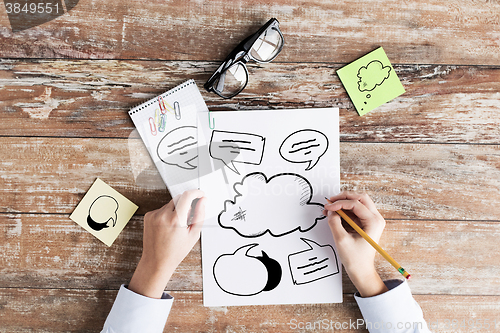 Image of close up of hands drawing text bubbles in notebook