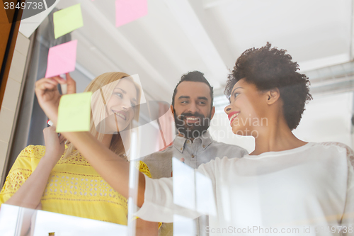 Image of happy creative team writing on stickers at office