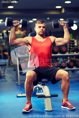 Image of young man with dumbbells flexing muscles in gym