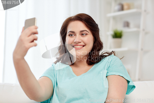 Image of happy plus size woman with smartphone at home