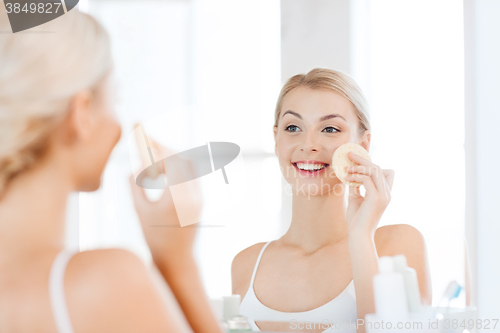 Image of young woman washing face with sponge at bathroom