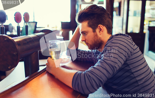 Image of unhappy lonely man drinking beer at bar or pub