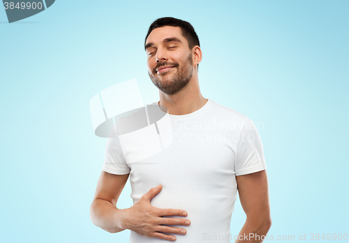 Image of happy full man touching tummy over blue background