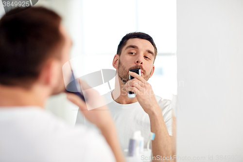 Image of man shaving mustache with trimmer at bathroom