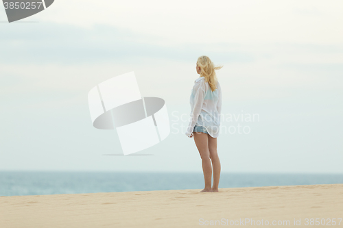 Image of Woman on sandy beach in white shirt at dusk. 
