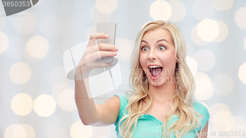 Image of smiling young woman taking selfie with smartphone