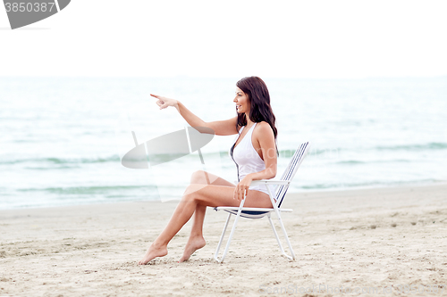 Image of smiling young woman sunbathing in lounge on beach