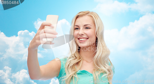 Image of smiling young woman taking selfie with smartphone