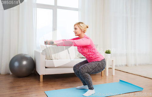 Image of smiling woman with dumbbells exercising at home