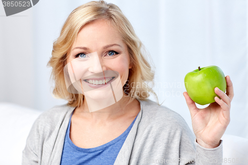 Image of happy middle aged woman with green apple at home