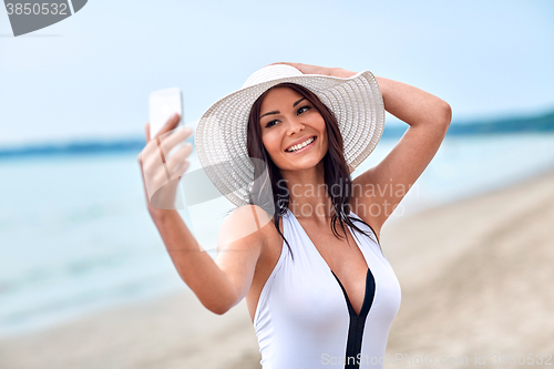 Image of smiling young woman taking selfie with smartphone