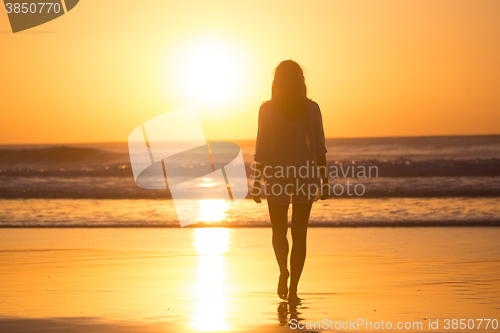 Image of Lady walking on sandy beach in sunset.